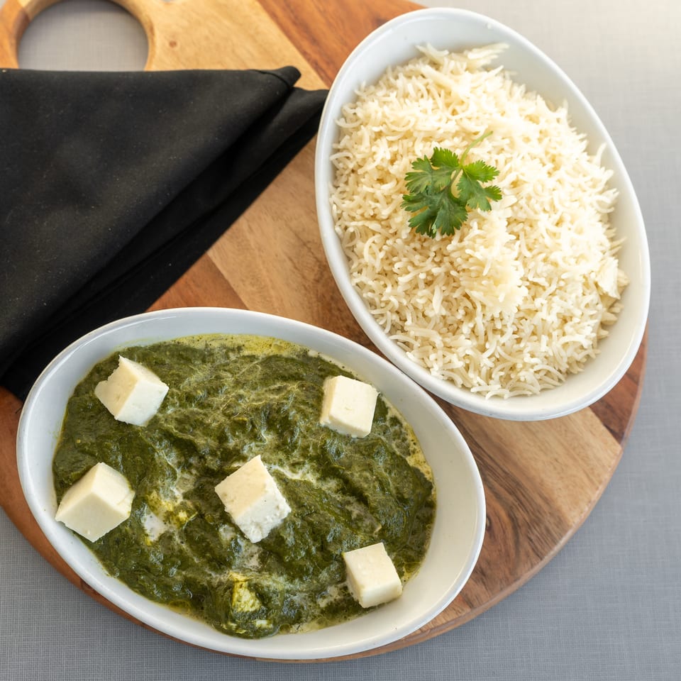 Overhead view of spinach paneer curry with white cheese cubes and basmati rice garnished with cilantro on a wooden serving board.