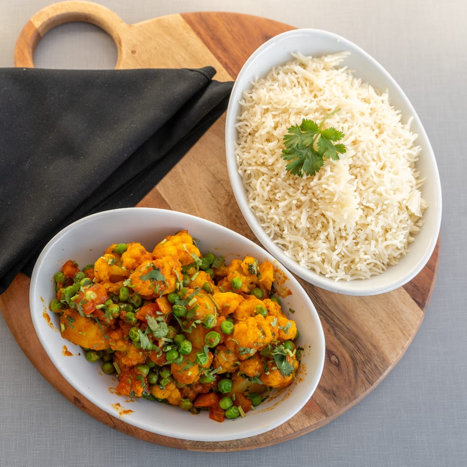Overhead view of basmati rice and vegetable curry garnished with cilantro, served on wooden boards beside a black napkin.