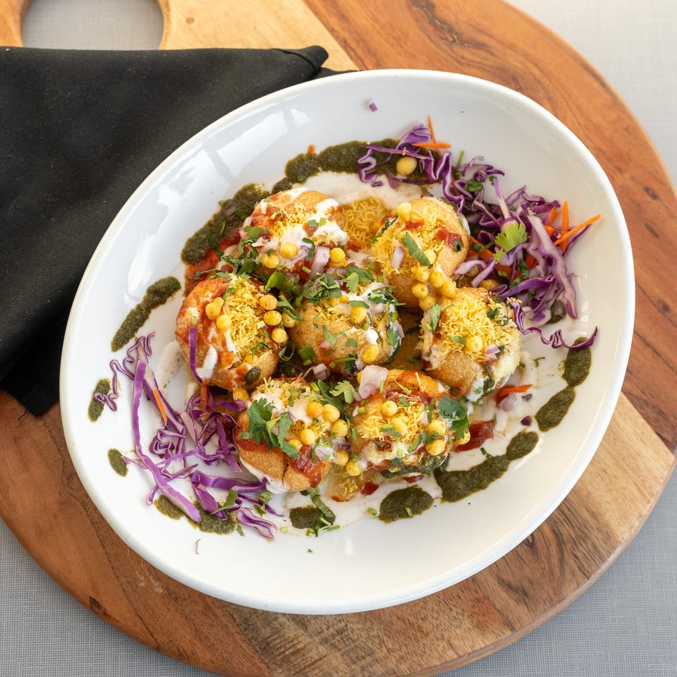 Indian chaat topped with yogurt, chutneys, sev, chickpeas, cilantro, and shredded cabbage on a white plate.