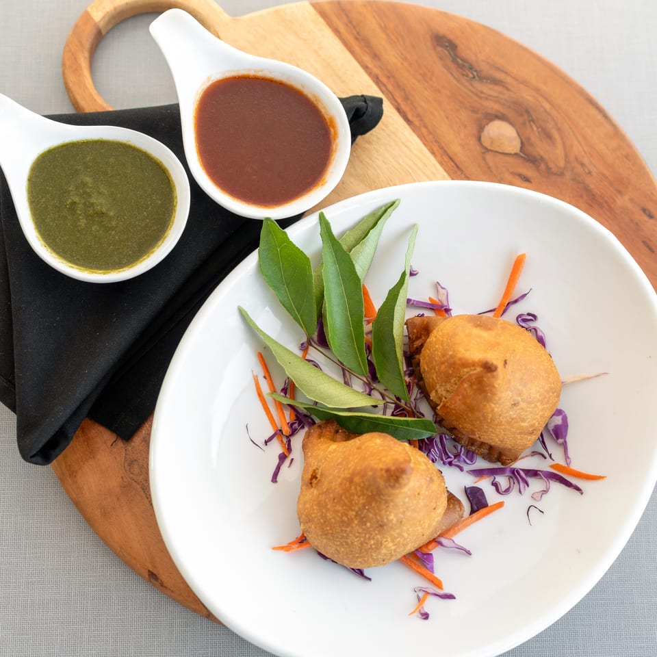 Crispy golden pastries served with shredded carrot and cabbage, leafy greens, and bowls of green and red dipping sauces.