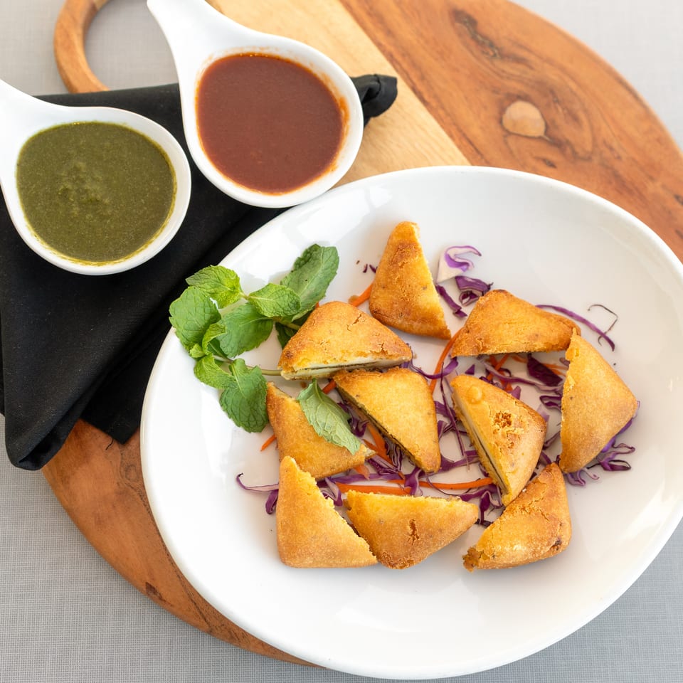 Golden fried triangular appetizers served with shredded cabbage, carrots, mint, and bowls of green and red dipping sauces.