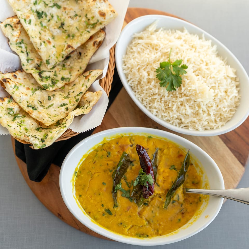 Indian meal with garlic naan, basmati rice, and yellow lentil curry garnished with herbs and dried chilies.