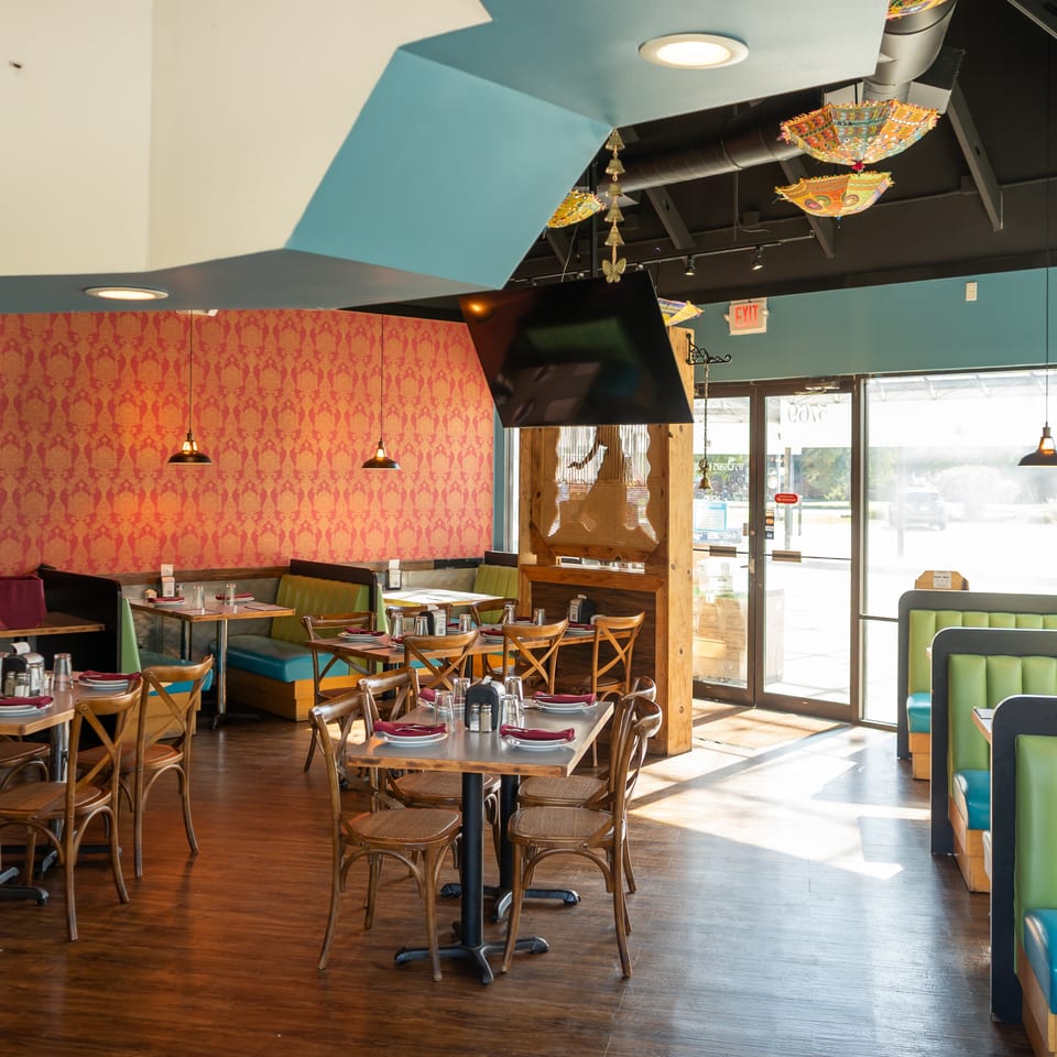 Colorful restaurant dining room with patterned walls, turquoise booths, set tables, pendant lights, and decorative hanging lanterns.